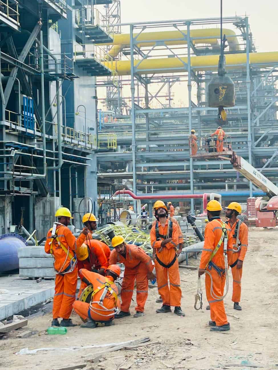 Industrial workers in orange coveralls and hard hats coordinating on a large petrochemical construction site